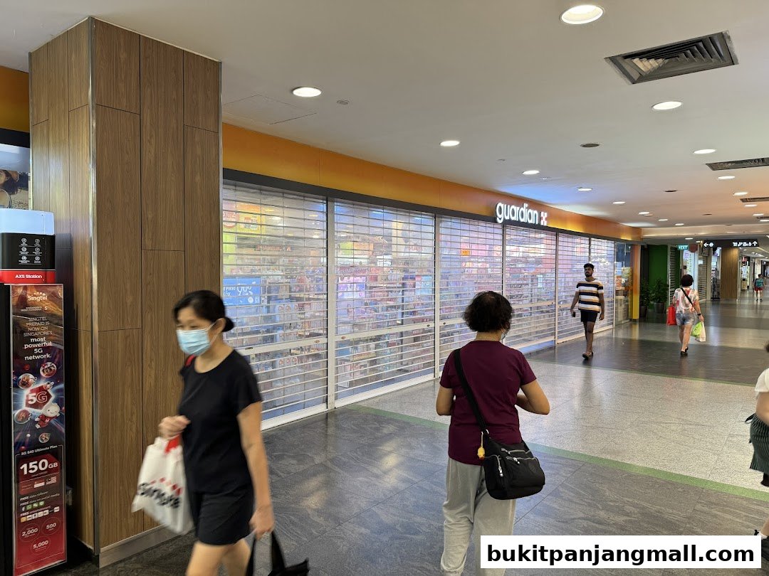 Guardian store front with roller shutters down, people walking in a mall.