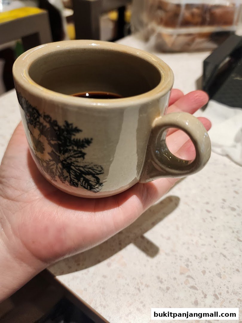 A hand holds a ceramic mug filled with dark coffee, featuring a nature-inspired design.