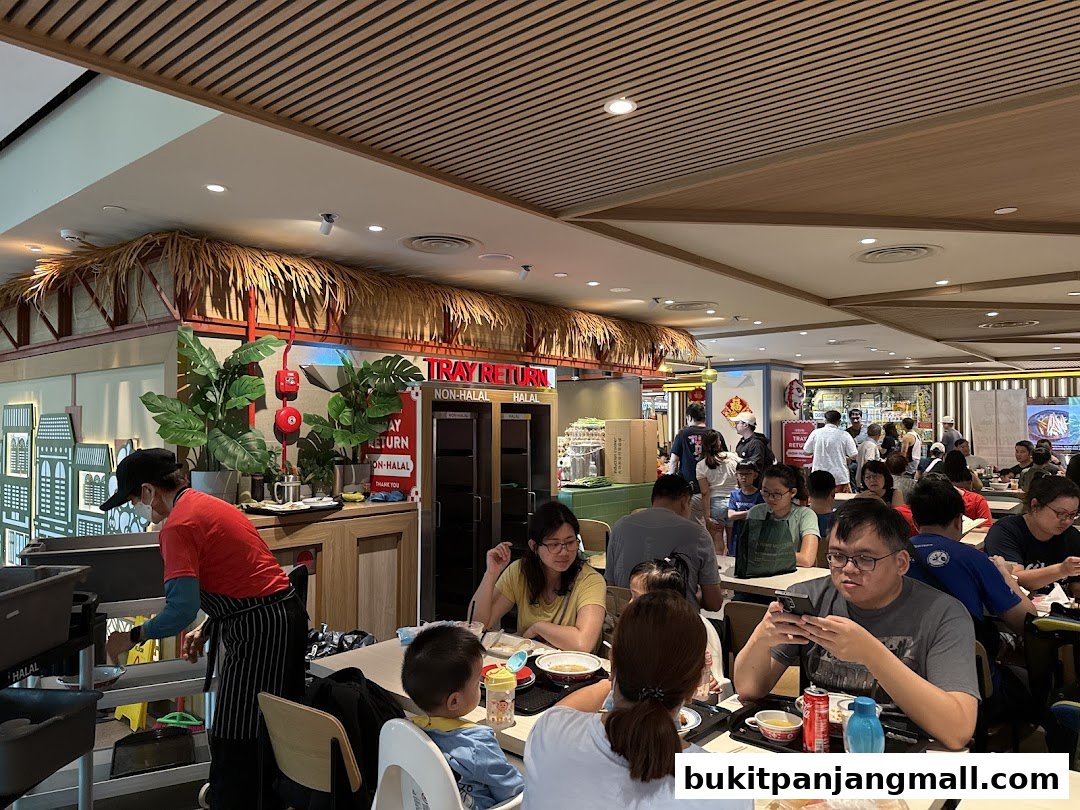 Diners enjoy meals at tables in a bustling food court with a tropical-themed decor.