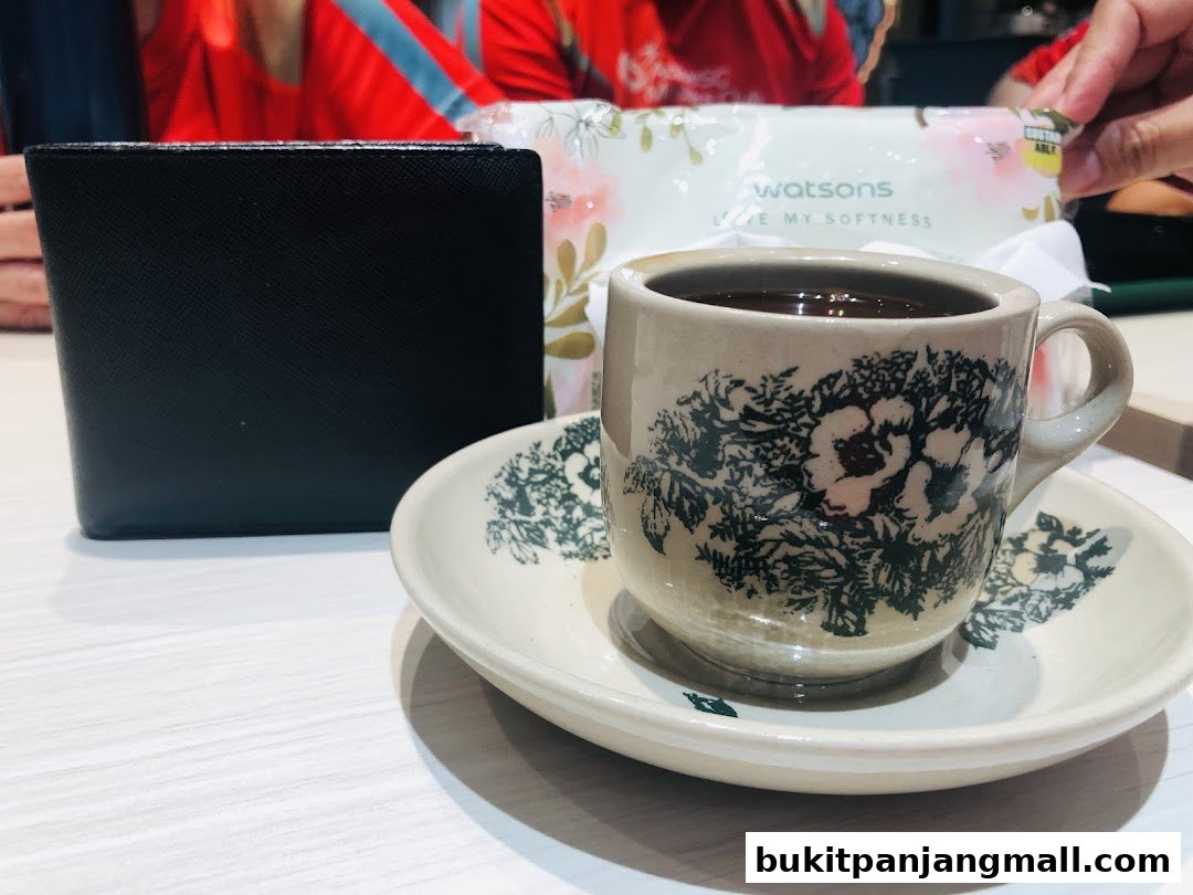 A black wallet and a cup of coffee on a saucer with a pack of Watsons wet wipes in the background.