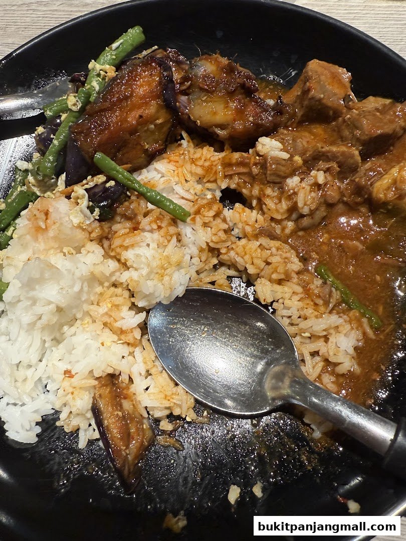 A close-up of a plate of rice with meat, vegetables, and a spoon.