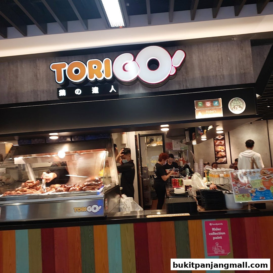 A busy food stall with staff serving customers and a display of grilled food.