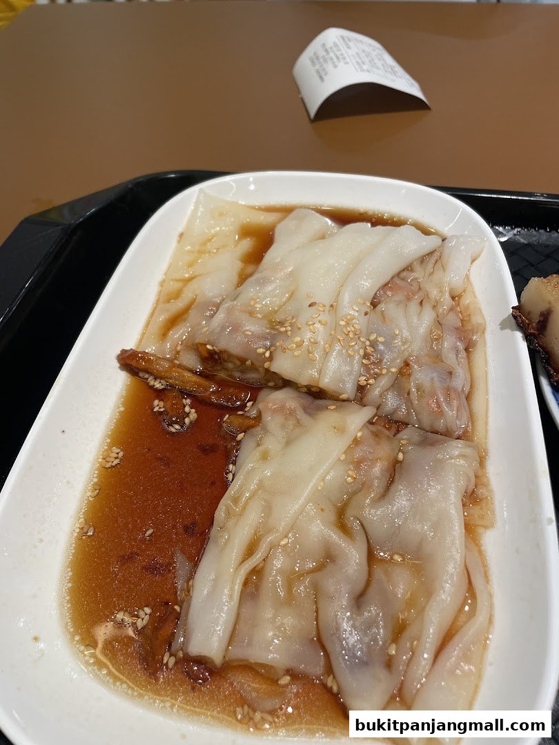 A close-up of steamed rice noodle rolls with sauce and sesame seeds.
