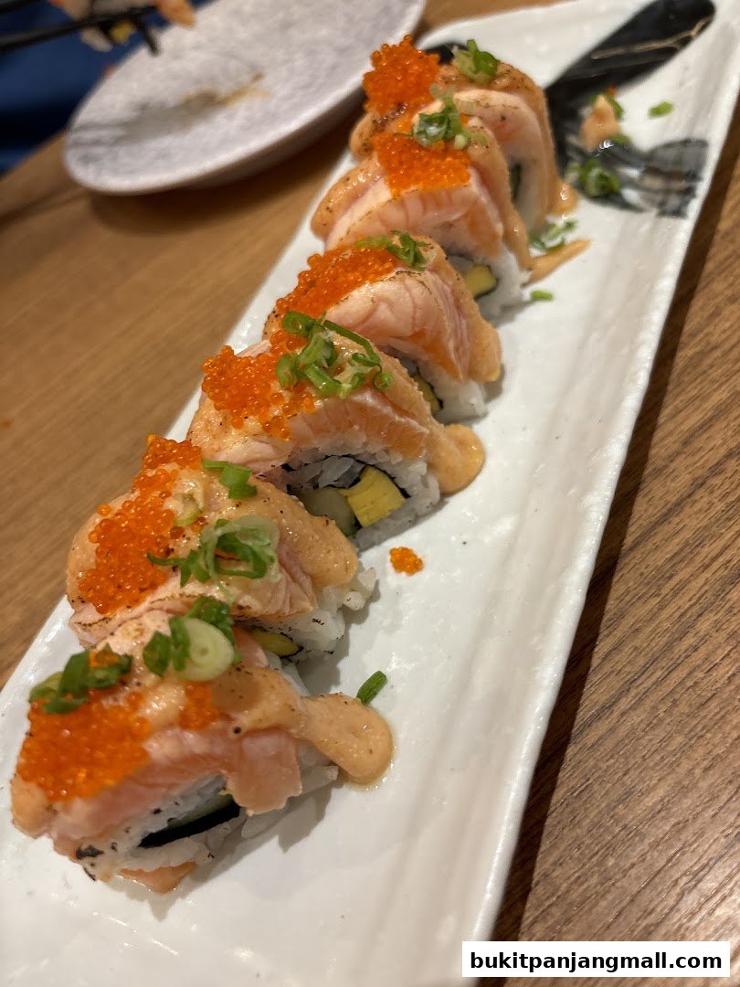 A close-up of a plate of salmon sushi rolls topped with roe and sauce.