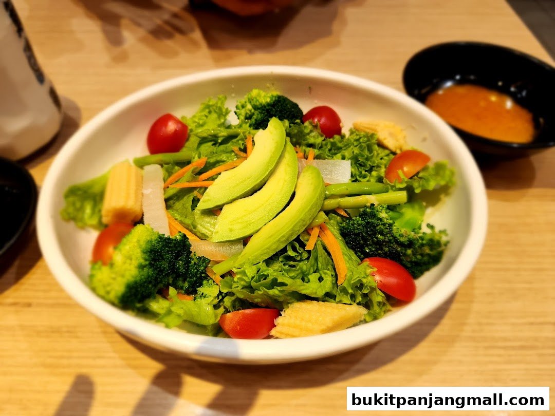 A fresh salad with avocado, broccoli, cherry tomatoes, and corn served in a white bowl.