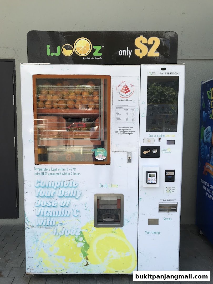 A white vending machine offering pure fruit juice, with oranges visible inside and lemon graphics on the front.