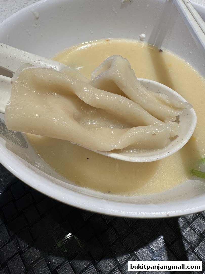 A close-up shot of Mee Hoon Kway being served in a white bowl with a spoon.