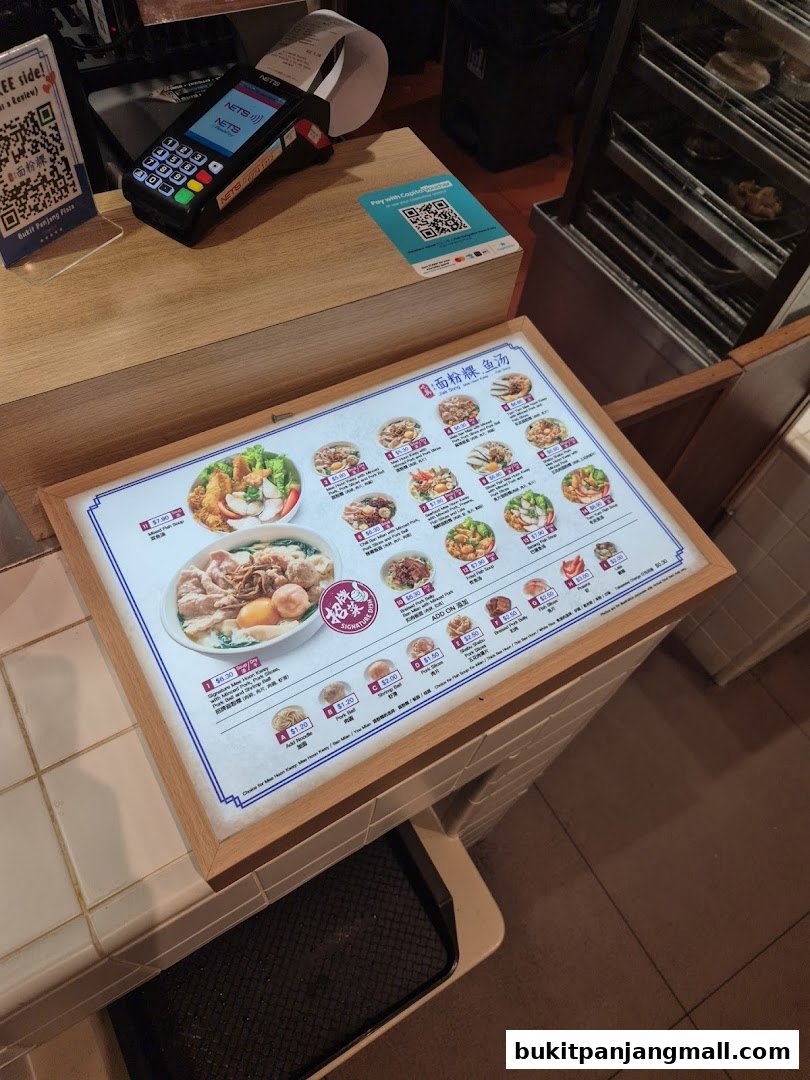A menu board displaying various noodle dishes and add-on items with prices.