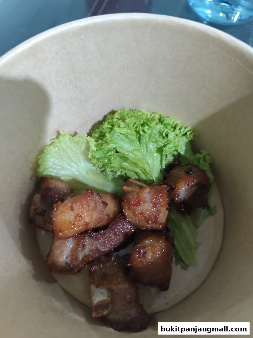 A close-up of braised pork belly with lettuce in a paper bowl.