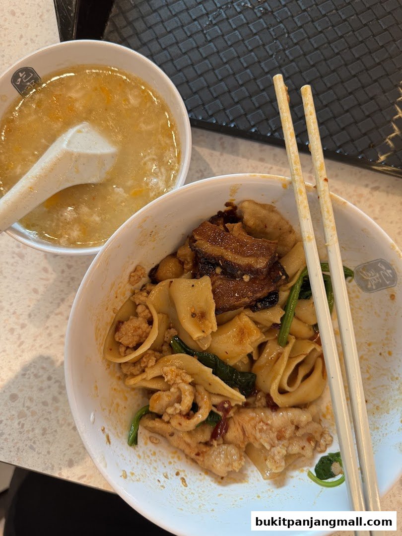 A bowl of mee hoon kway with minced meat, pork belly, and vegetables, served with soup.