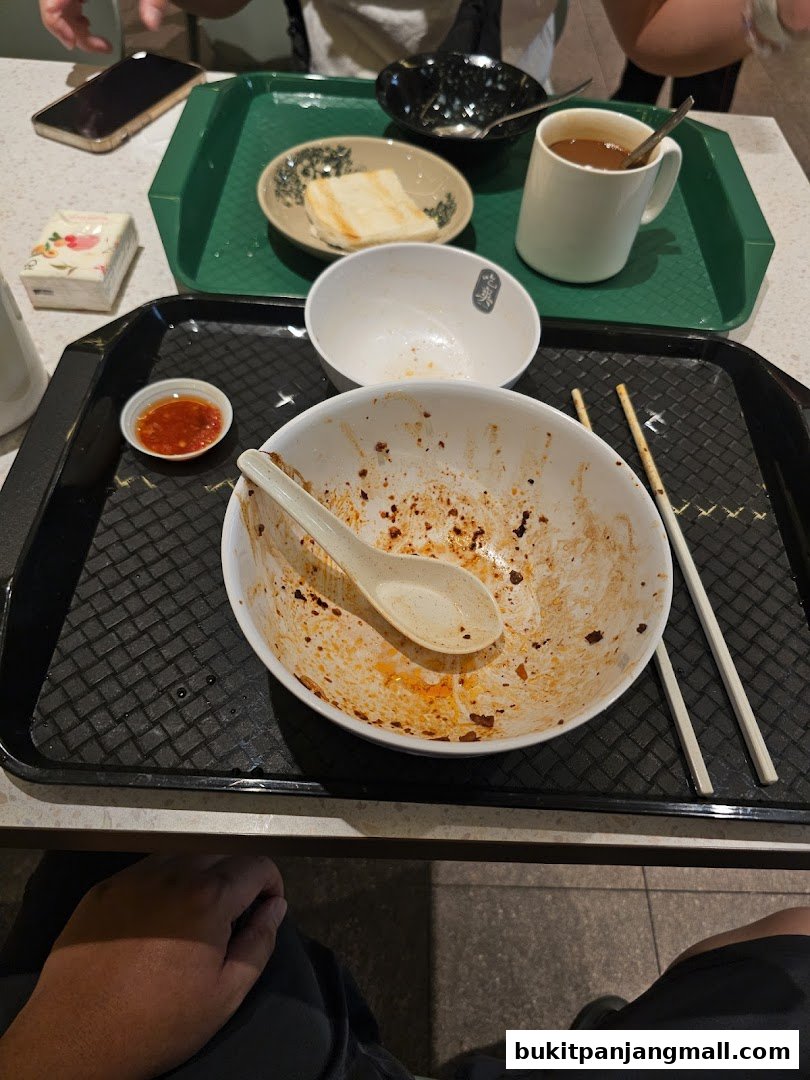 A close-up of a nearly empty bowl of noodles with chili sauce and a spoon.