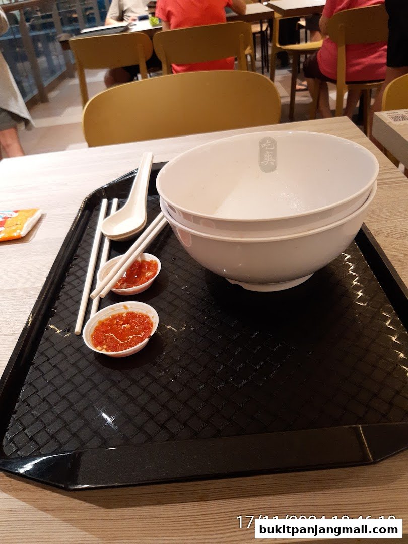 A tray with two bowls, chopsticks, a spoon, and two small dishes of chili sauce.