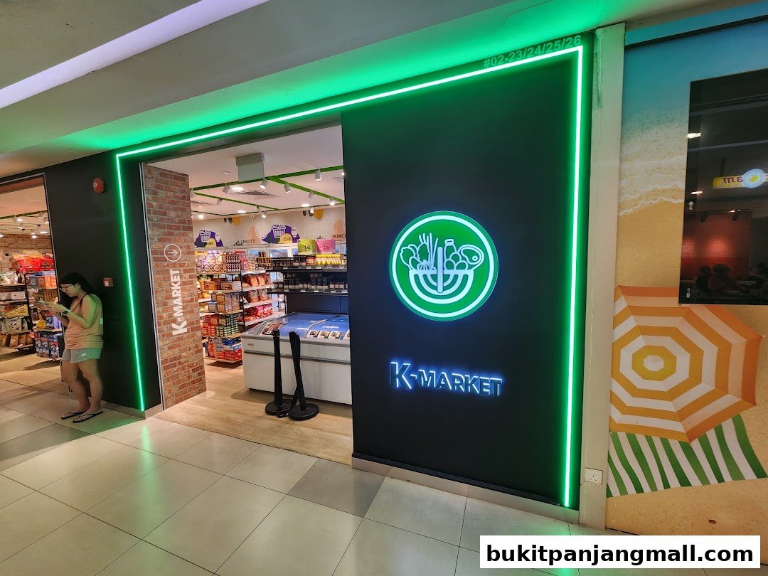 The entrance of K-MARKET, a Korean grocery store, illuminated by green neon lights.