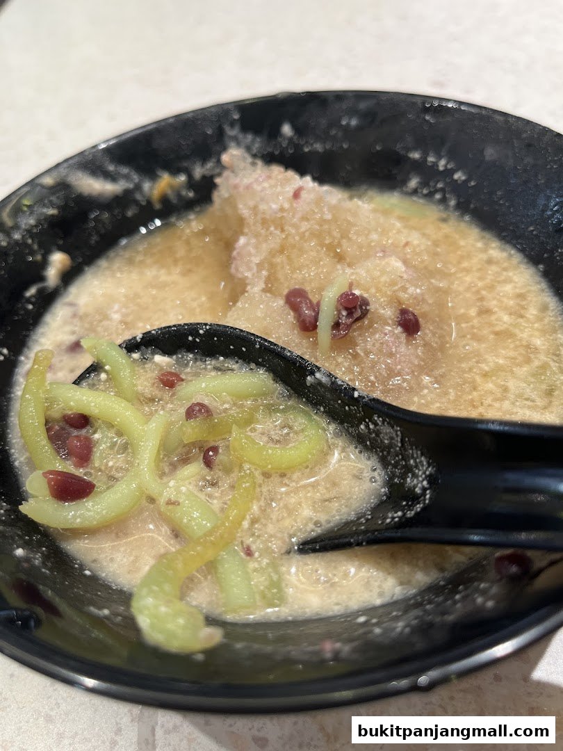 A close-up shot of a bowl of Cendol dessert with a spoon.