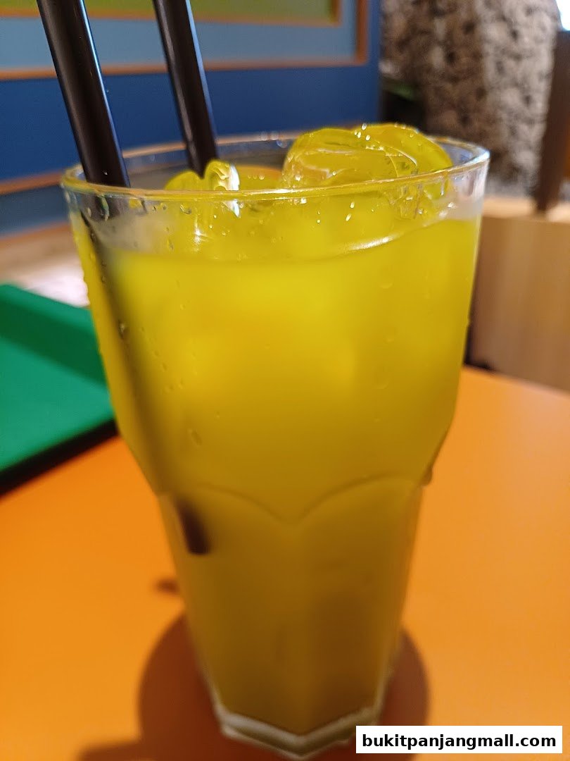 A refreshing yellow beverage with ice and two black straws in a glass.