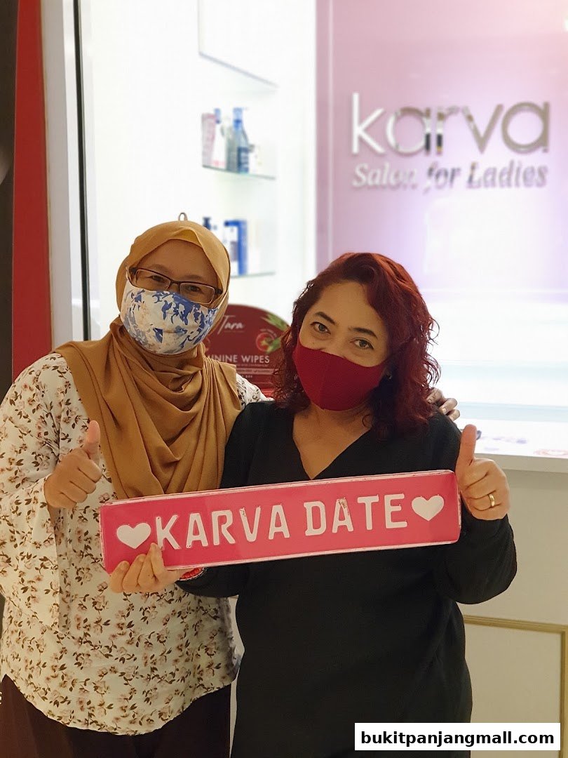 Two women posing with a 'KARVA DATE' sign in front of a salon.