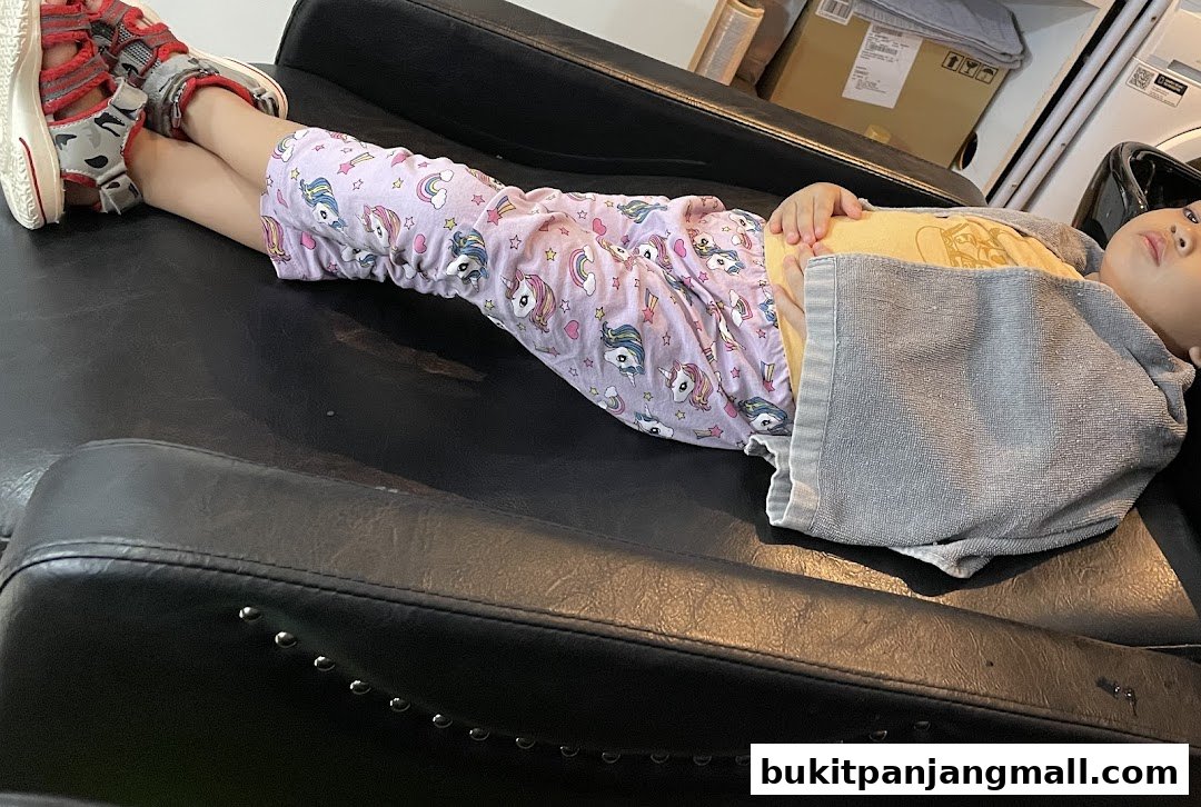 A child in unicorn pajamas rests on a salon chair with a towel draped over them.