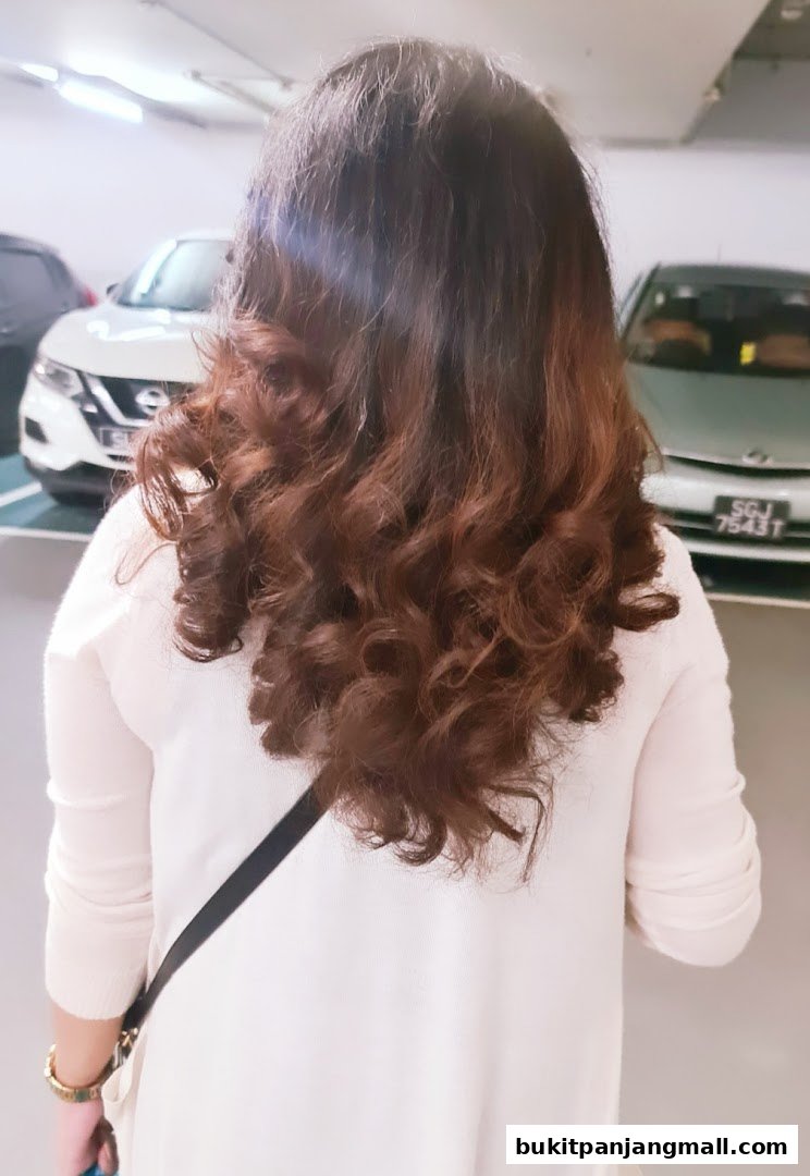 A woman with long, wavy brown hair is shown from behind in a parking lot.