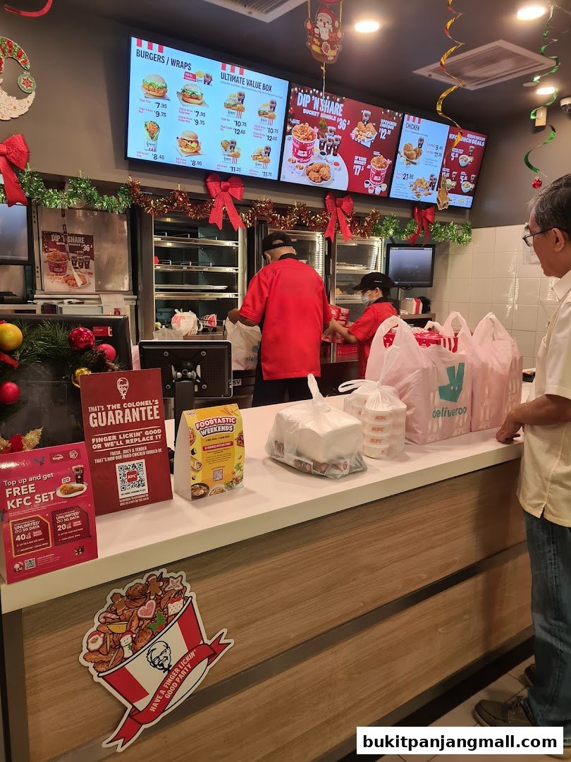 KFC counter with digital menus displaying food items and staff serving customers.