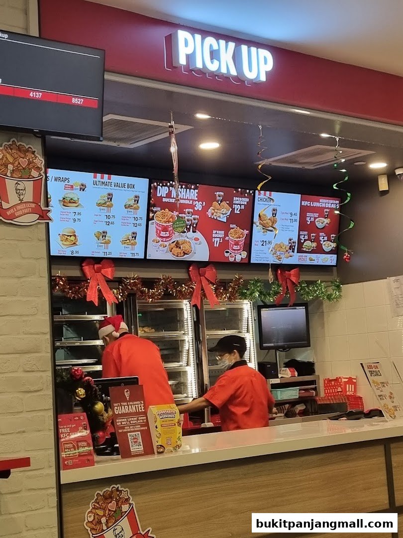 KFC counter with digital menus displaying food items and staff serving customers.