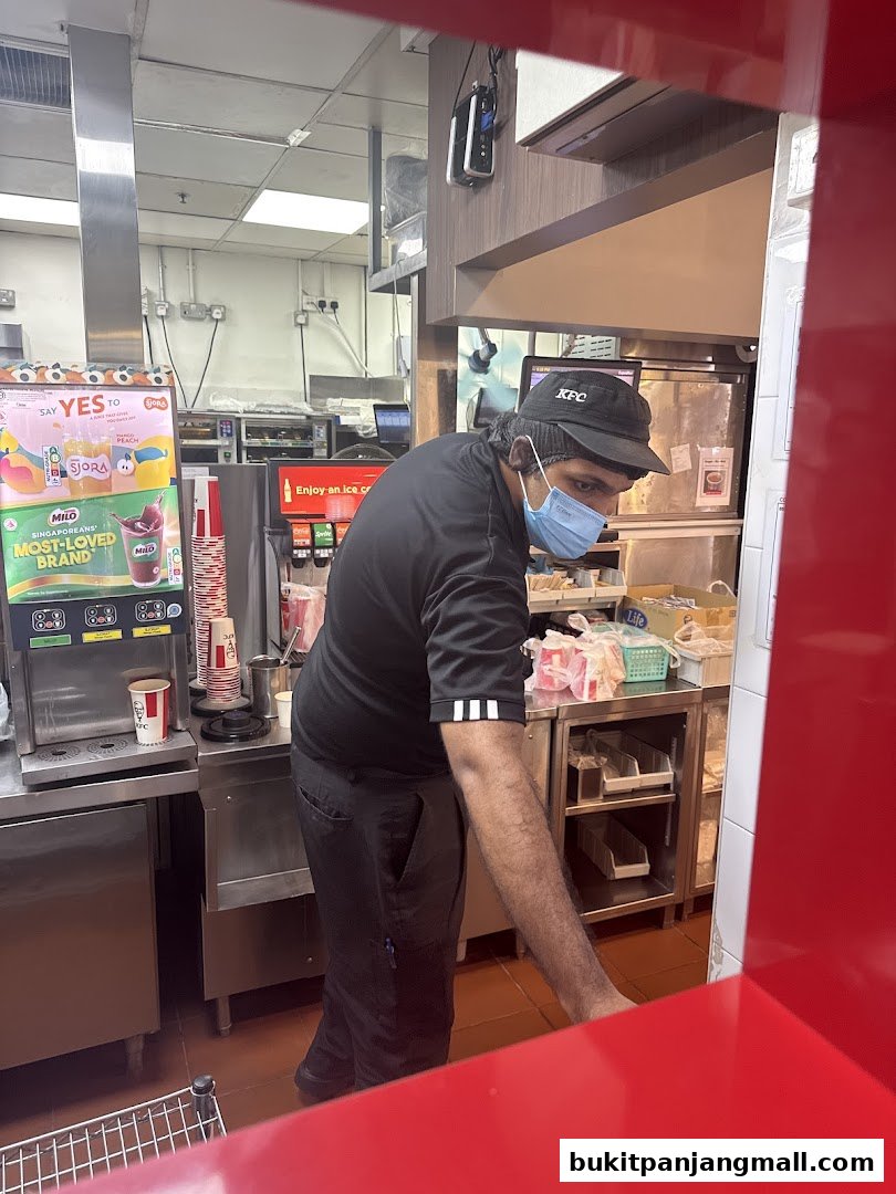 A KFC employee wearing a mask and cap works behind the counter.