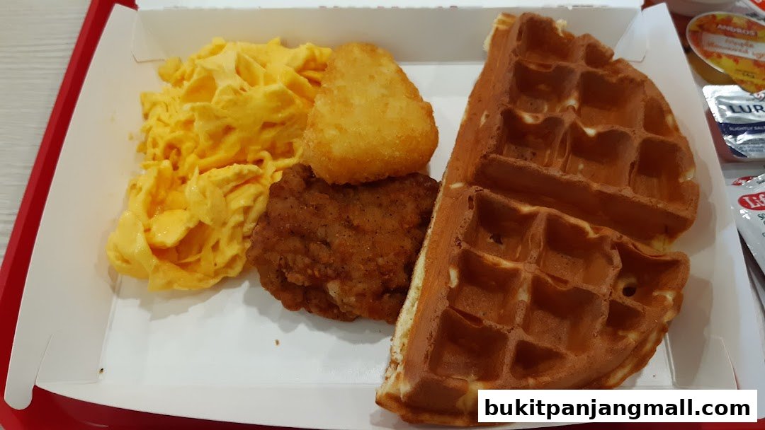 A close-up of a KFC breakfast meal with scrambled eggs, fried chicken, hash brown, and a waffle.