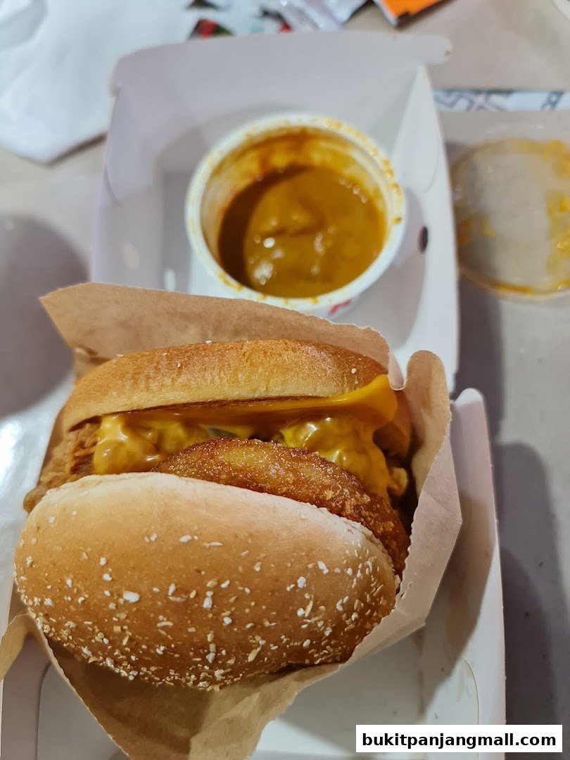 A close-up of a KFC burger with cheese and a side of curry sauce.