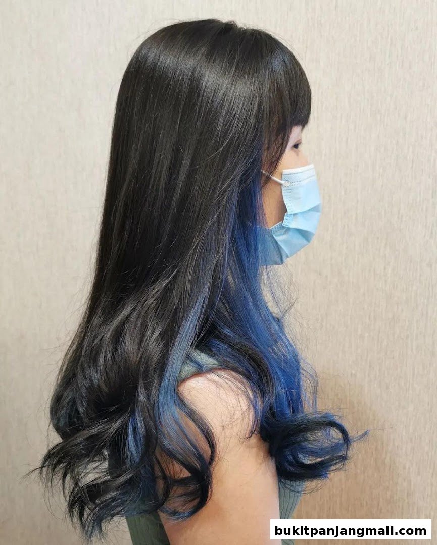 A woman with long, dark, wavy hair with blue highlights, wearing a face mask.