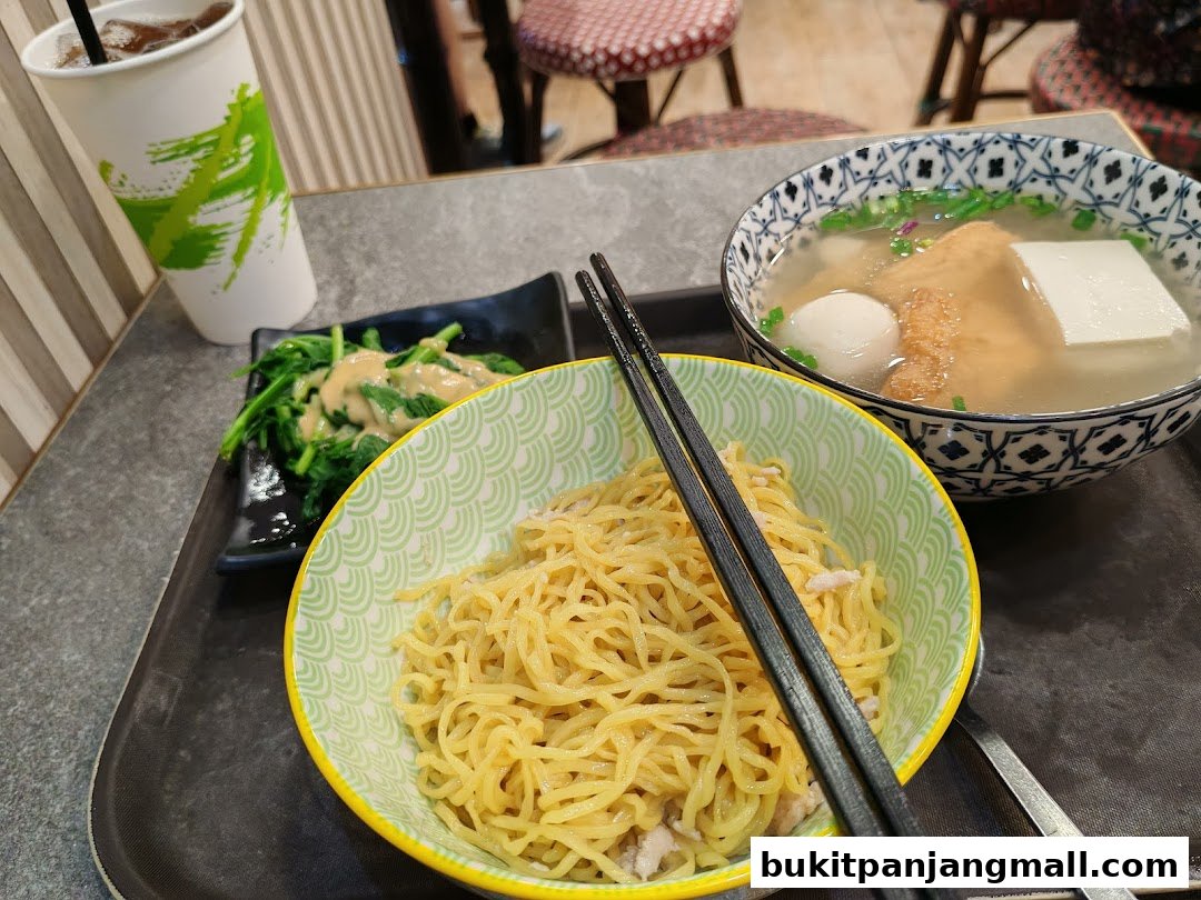 A close-up of a delicious meal featuring noodles, soup with fish balls and tofu, and a side of greens.