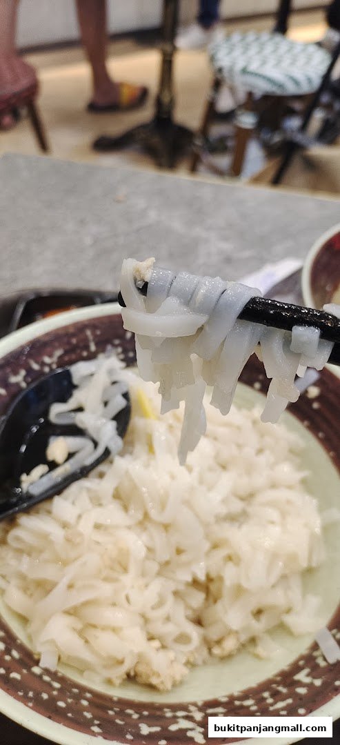 A close-up shot of a bowl of noodles being lifted with chopsticks.