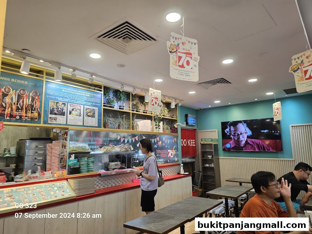 Interior of a Koo Kee restaurant with customers and a display of awards and heritage.