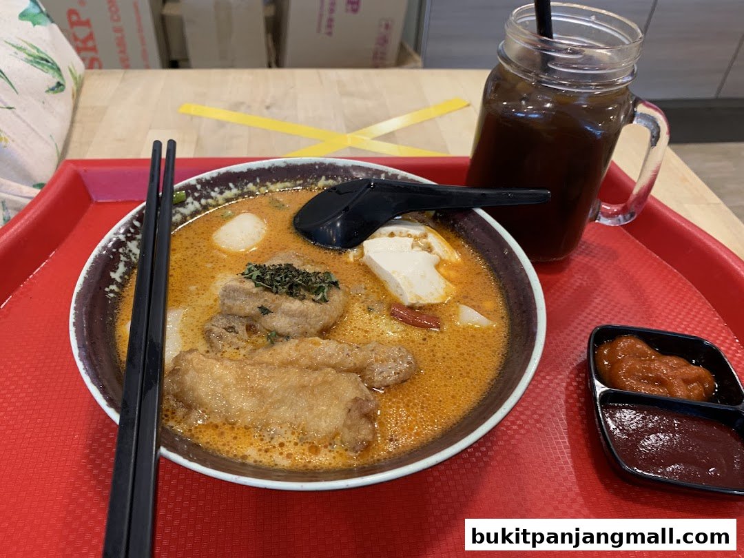 A bowl of curry noodle soup with a drink and dipping sauces on a red tray.