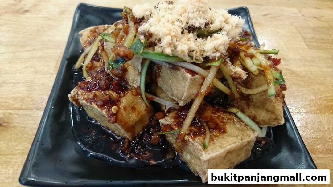 A plate of crispy fried tofu cubes topped with shredded meat, cucumber, and a savory sauce.