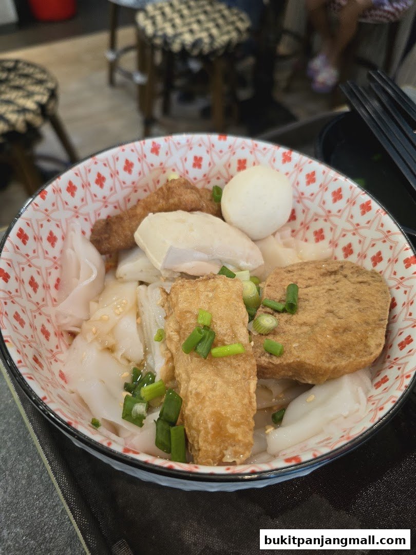 A close-up of a bowl of noodles with various toppings including fish balls and fried tofu.
