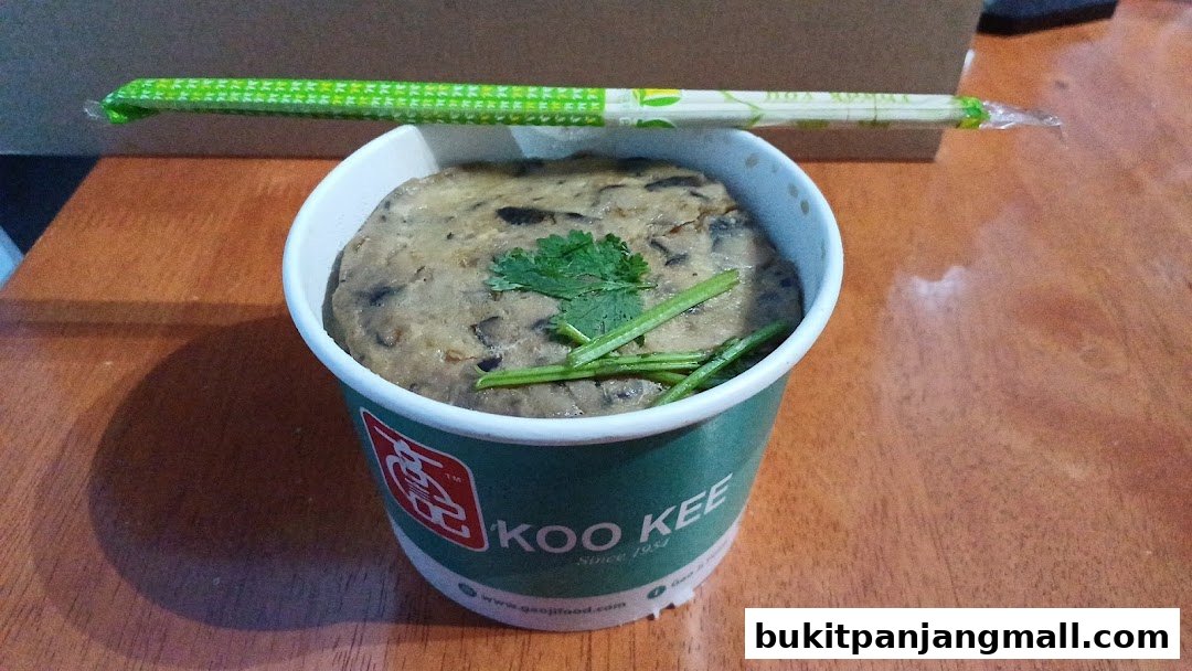 A cup of Koo Kee food with chopsticks on top, garnished with cilantro and green onions.