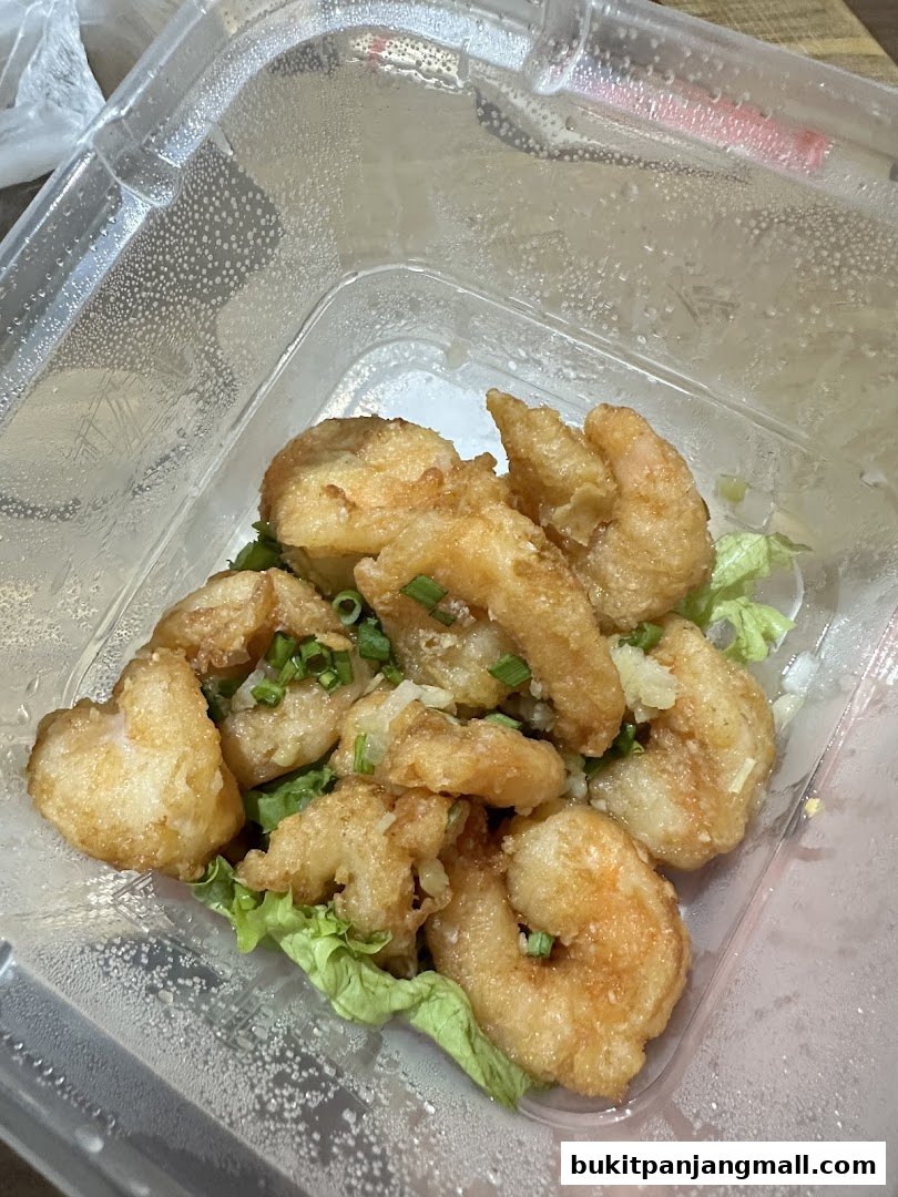 A close-up of crispy fried shrimp with green onions in a clear takeout container.