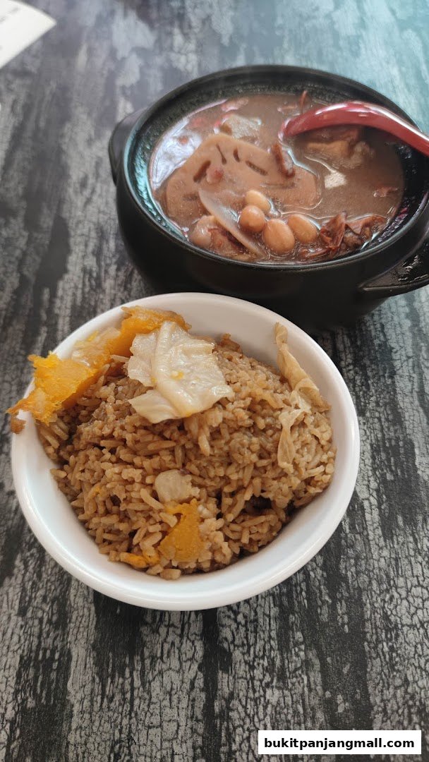 A bowl of rice topped with vegetables sits next to a pot of soup with lotus root and peanuts.