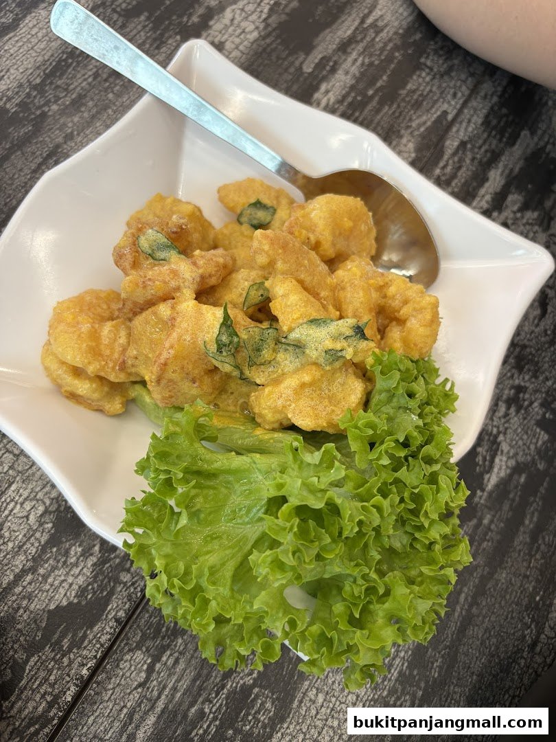 A white bowl filled with golden fried shrimp and garnished with lettuce and curry leaves.
