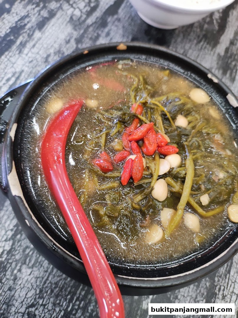 A close-up of a steaming bowl of herbal soup with vegetables and goji berries.