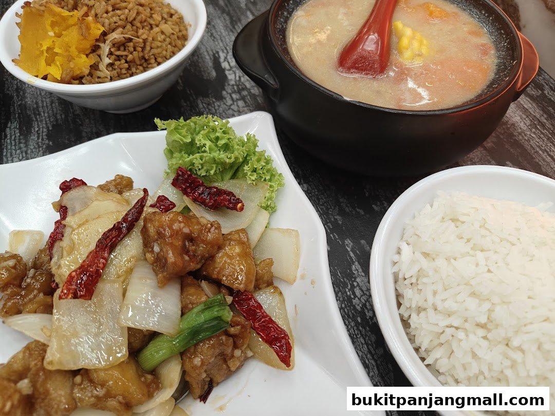 A close-up shot of a delicious meal featuring stir-fried chicken with dried chilies and onions, rice, and a bowl of soup.