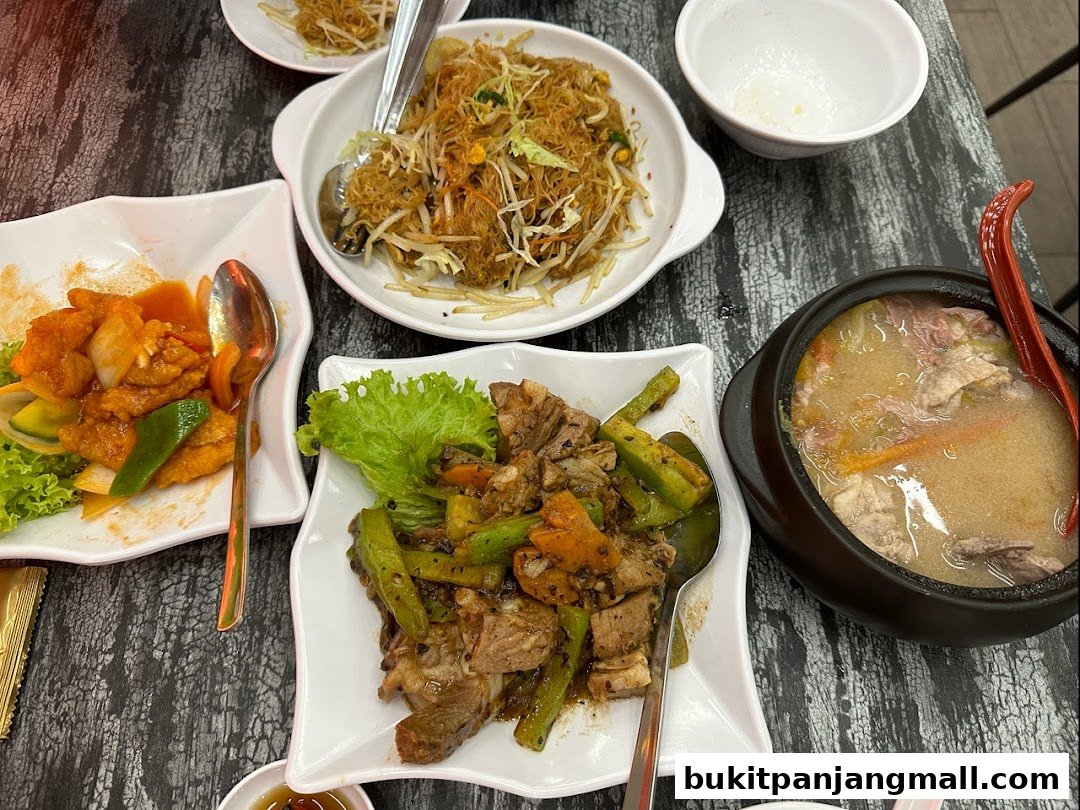A table laden with various delicious Asian dishes, including stir-fried noodles, sweet and sour chicken, and a hearty soup.