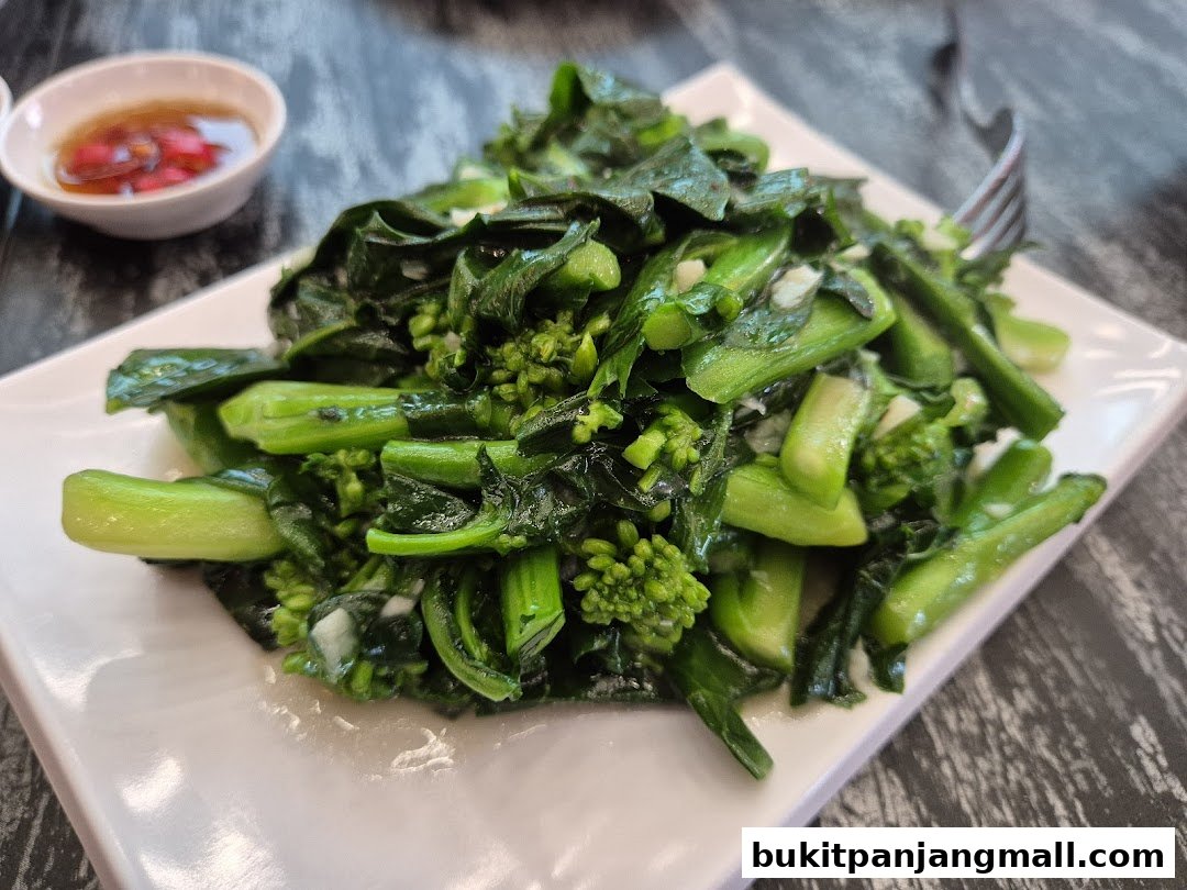 A plate of stir-fried green vegetables with garlic and a side of dipping sauce.
