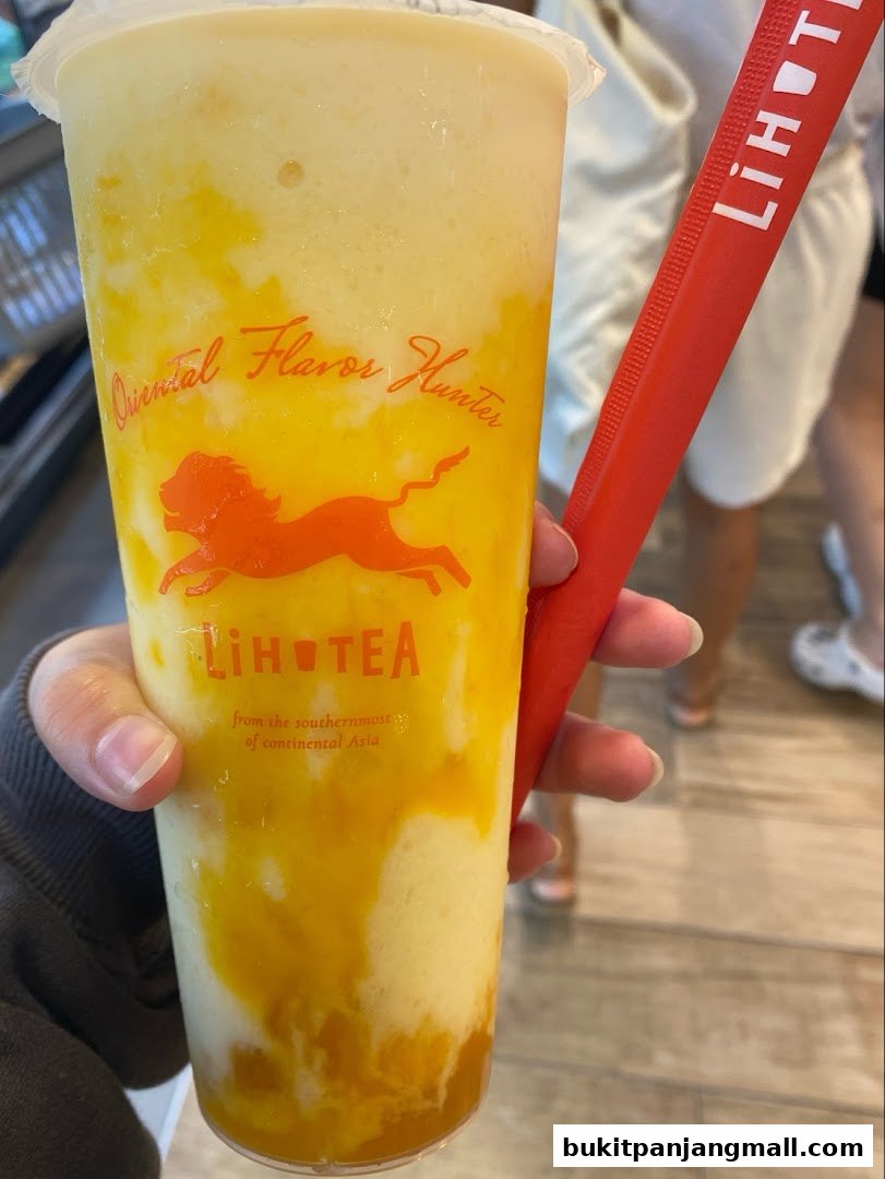 A hand holds a large cup of LiHO TEA with a mango-like swirl and a red straw.