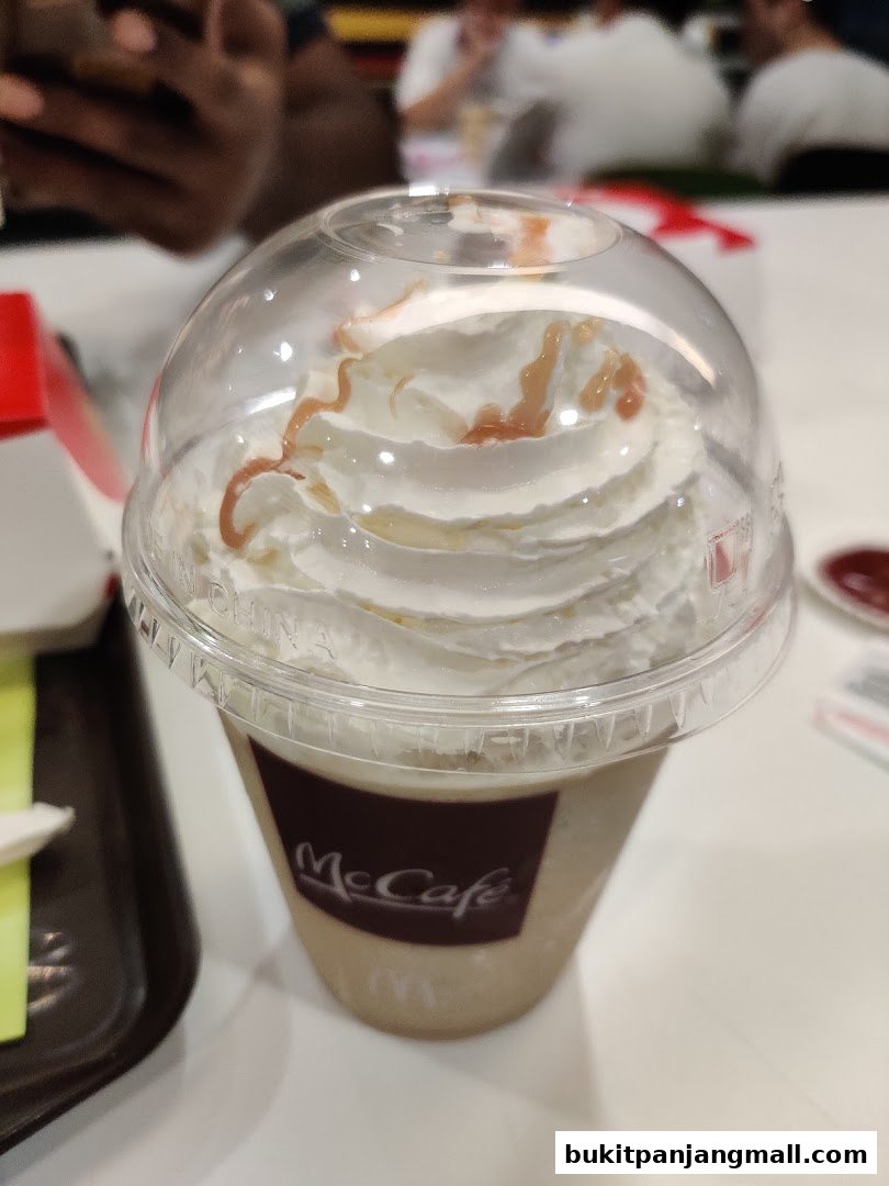 A close-up of a McCafe drink topped with whipped cream and caramel drizzle.
