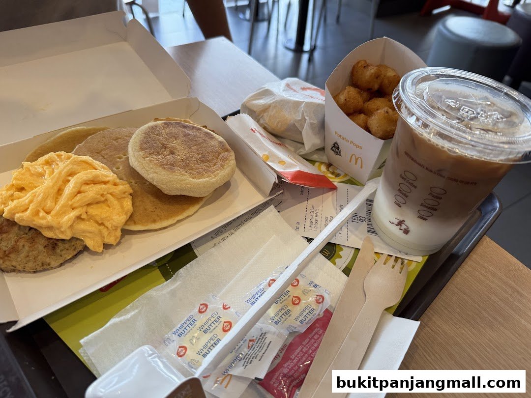 A tray of McDonald's breakfast items including pancakes, scrambled eggs, a burger, potato pops, and iced coffee.