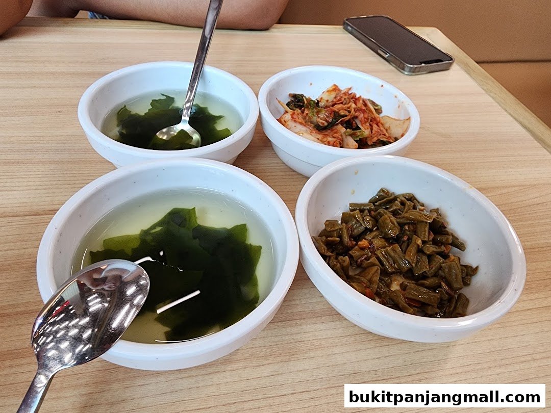 Four bowls of Korean side dishes and soup are arranged on a wooden table.