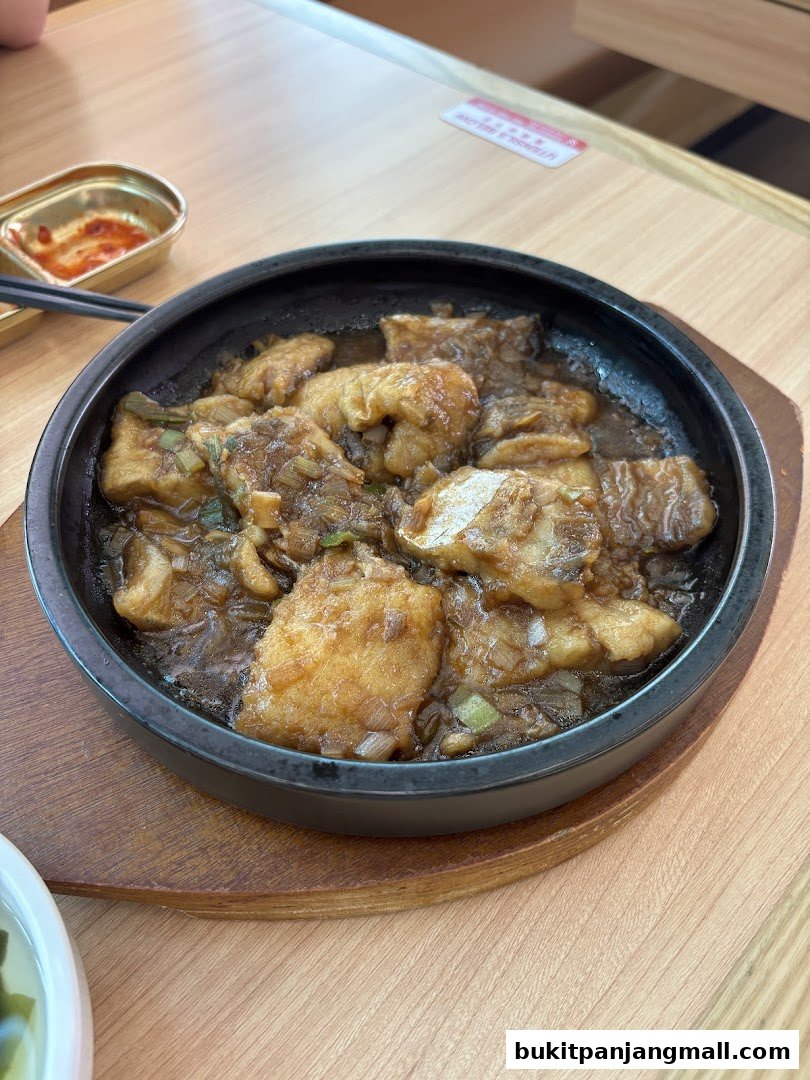 A close-up shot of a sizzling dish of fish in a dark bowl on a wooden table.