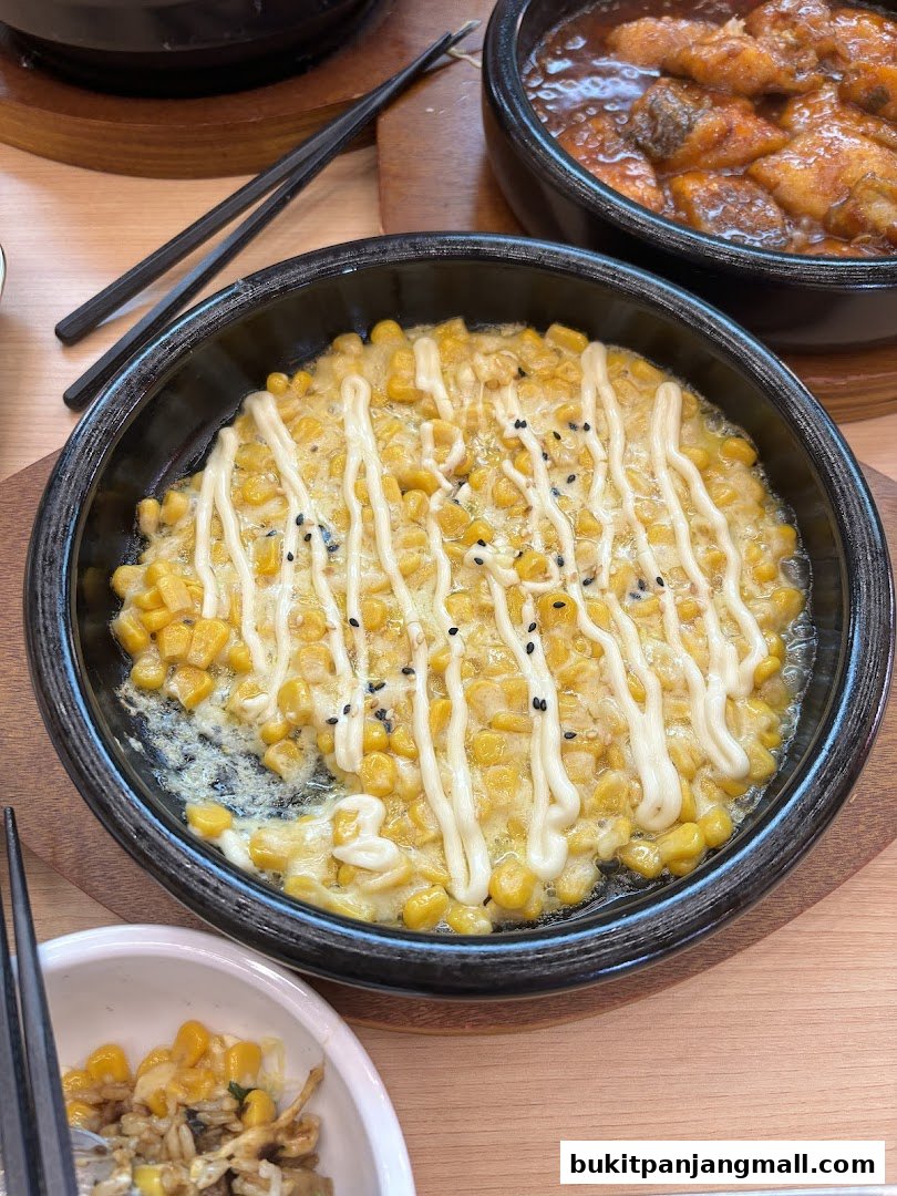 A close-up of a dish with corn and mayonnaise, served in a black bowl with chopsticks.