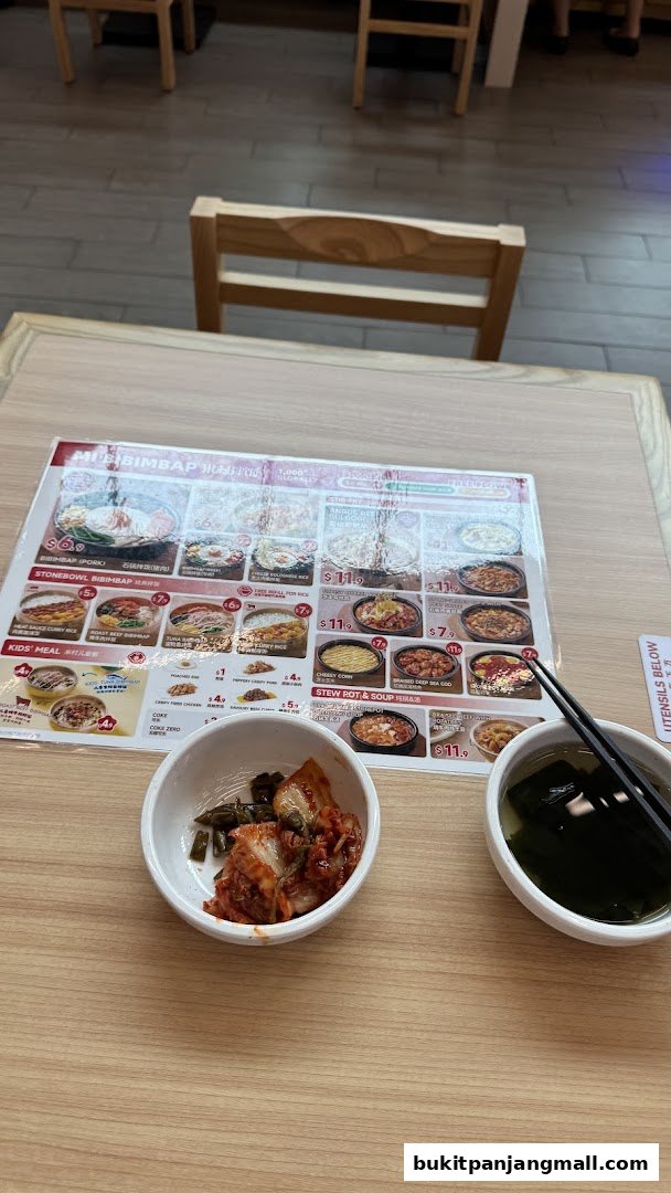 A table at Micun Bibimbap with a menu, kimchi, and soup.