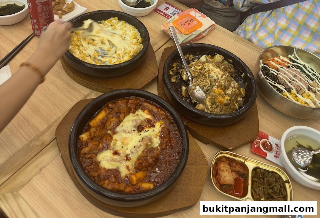 A table laden with various Korean dishes, including bibimbap, tteokbokki, and corn cheese.